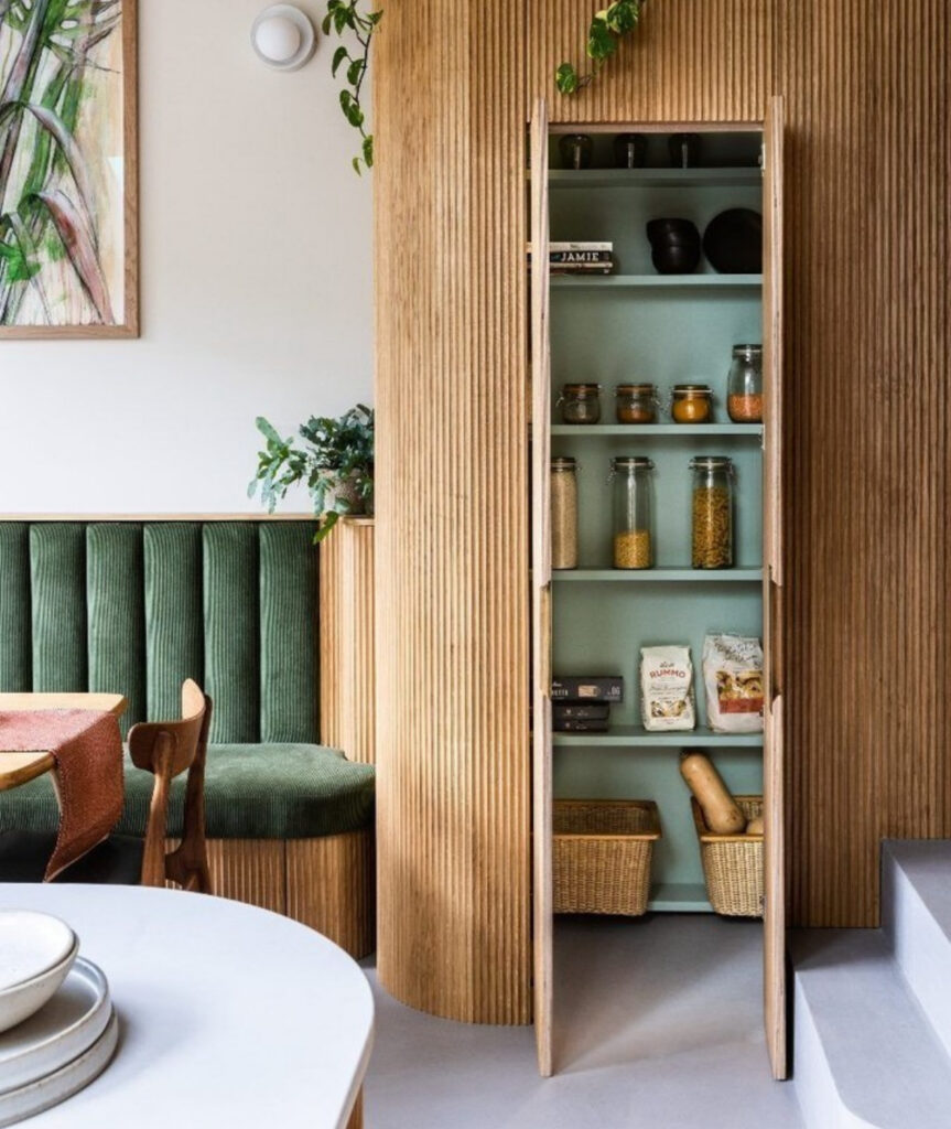 fluted wood column in a dining nook conceals a mint green interior cabinet that opens into a hidden small walk in pantry for jars and baskets