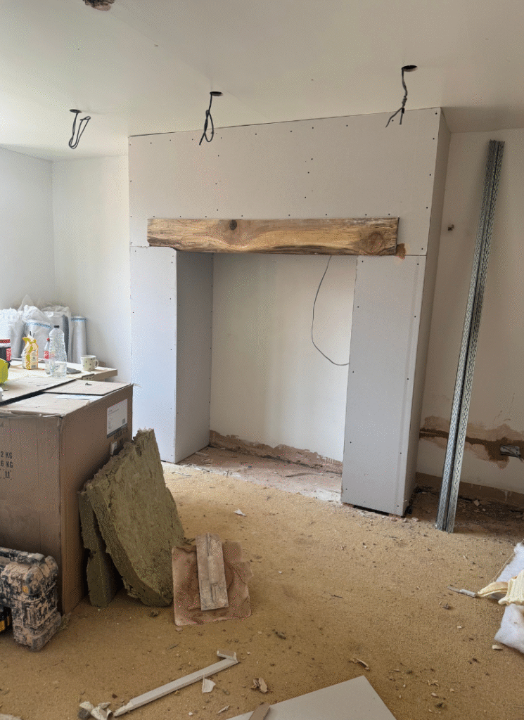 Early stage faux inglenook fireplace with plasterboard surround and rustic beam, inspiring barn conversion ideas for characterful focal points.