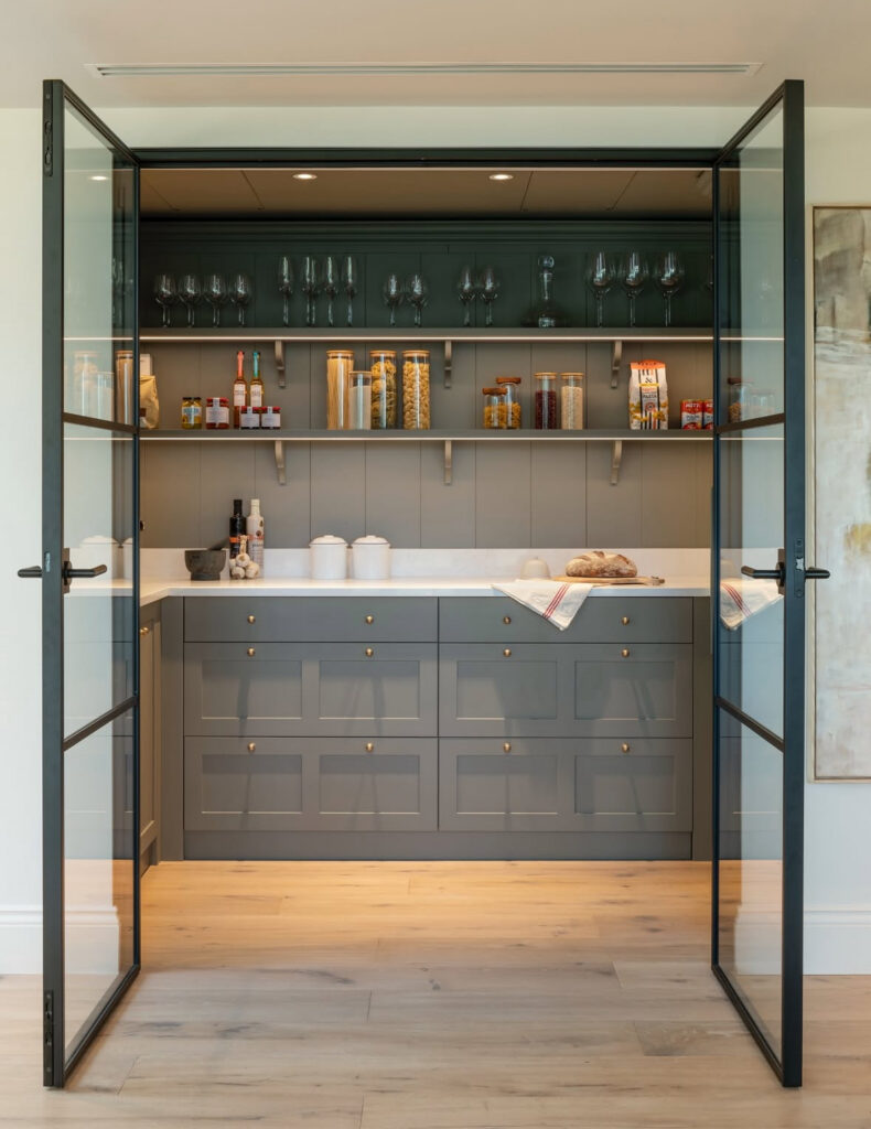 steel framed glass doors slide open to a spacious walk in kitchen pantry with long counters and open shelving