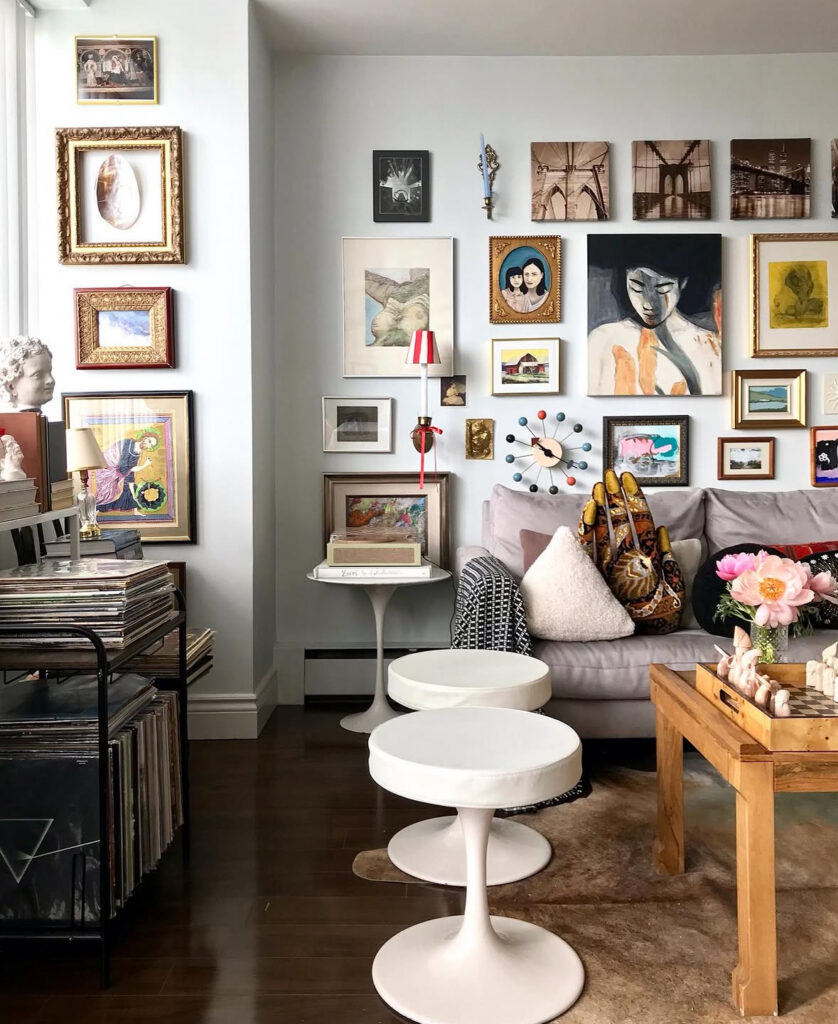 Living room with layered gallery wall, tulip tables, and record collection, showing an artistic mix of textures in eclectic home decor.