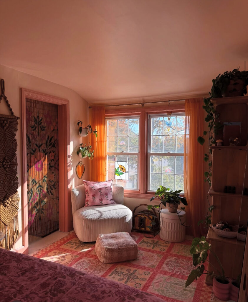 Cozy boho bedroom corner with soft pink walls, patterned rug, and plants by the window, inspiring peaceful eclectic home decor ideas.
