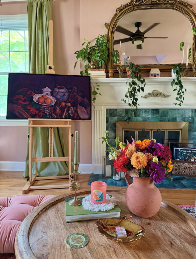 Elegant pink living room with green curtains, ornate mirror, and bright flowers — classic and modern eclectic home decor combined.