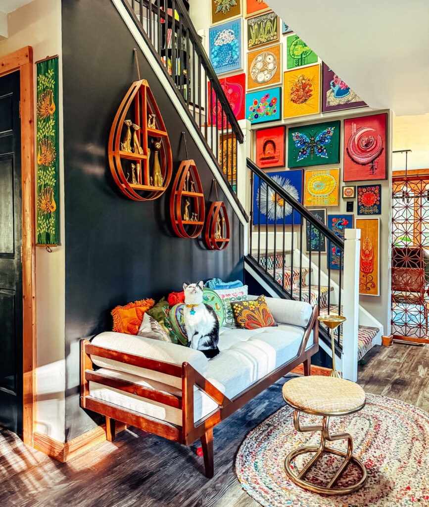Staircase with colorful gallery wall, mid-century bench, and dark-painted backdrop — bold, layered eclectic home decor style in action.