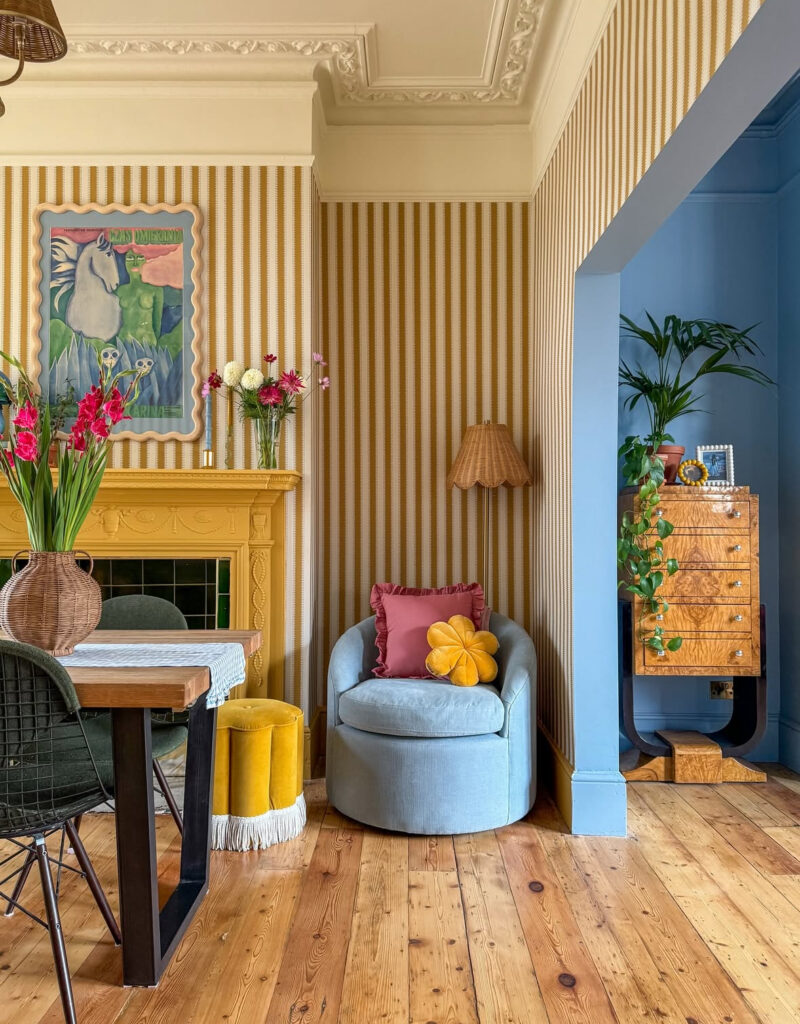 Bold living room with yellow striped wallpaper, blue armchair, and colorful accents, showing playful layers of eclectic home decor.