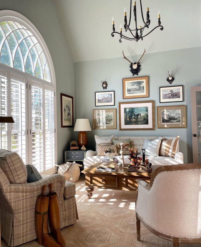 Plaid chair, wood coffee table, and equestrian art create a tailored french country living room with a tall arched window.