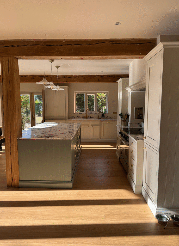 Light-filled country kitchen with exposed beams, marble island, and sage cabinetry, showcasing elegant barn conversion ideas.