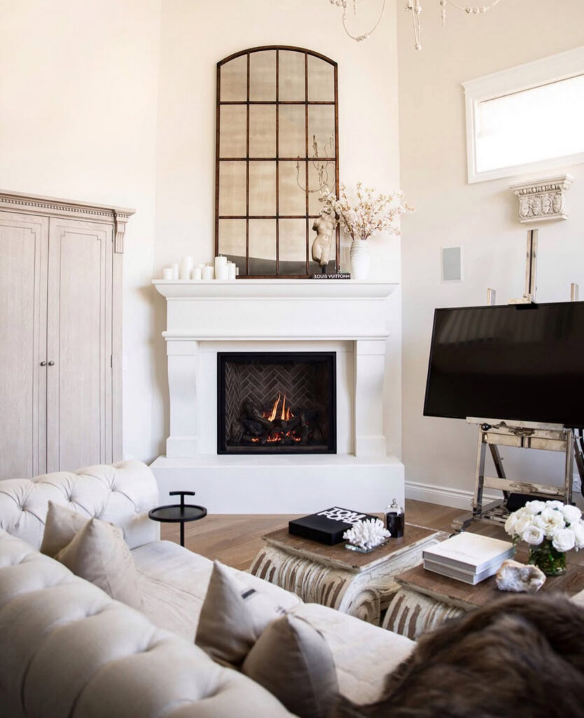 Tufted sofa, sculptural coffee tables, and a tall arched mirror above the fireplace show a streamlined take on french country interior design.