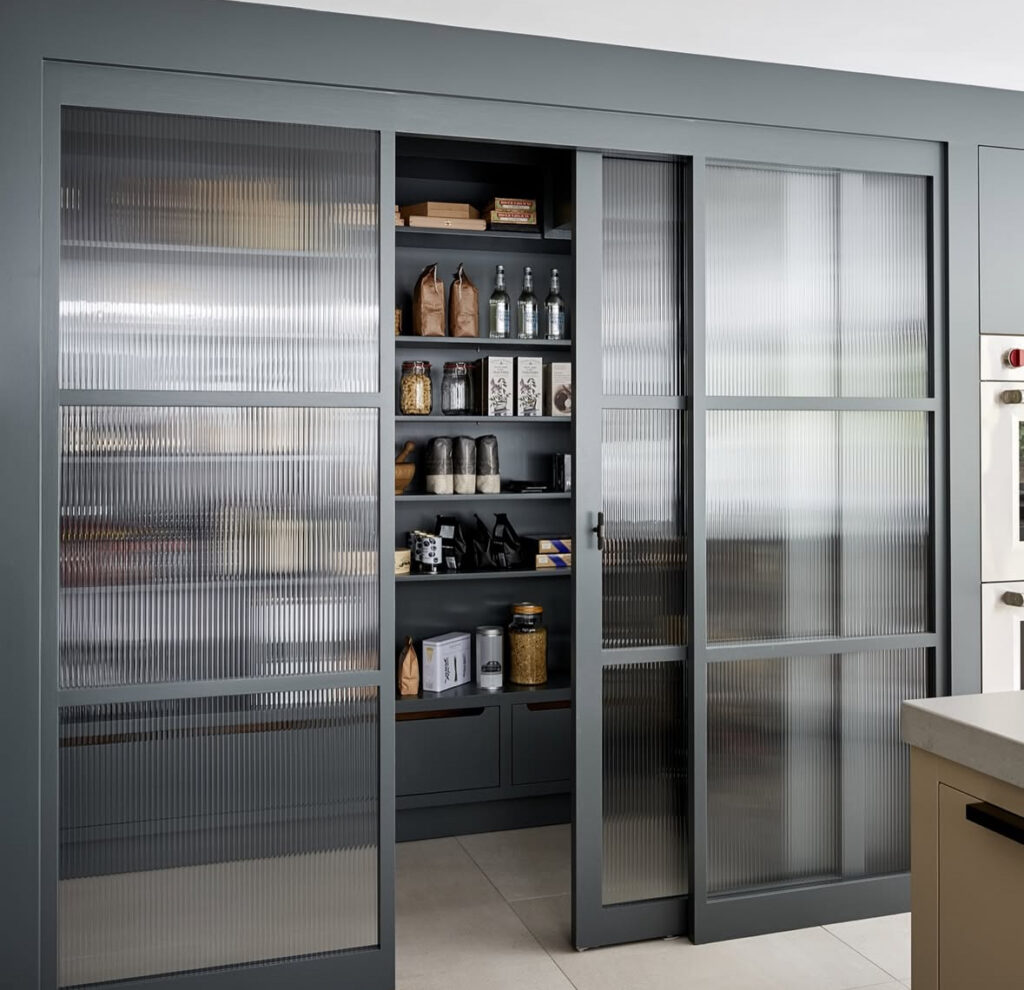 large sliding ribbed glass doors reveal a full wall of walk in pantry shelves filled with jars and bottles