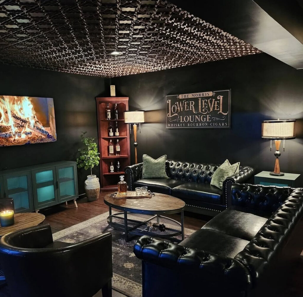 Dark walls, tufted leather sofas, and a patterned ceiling bring dramatic black man cave ideas to this lower-level lounge.