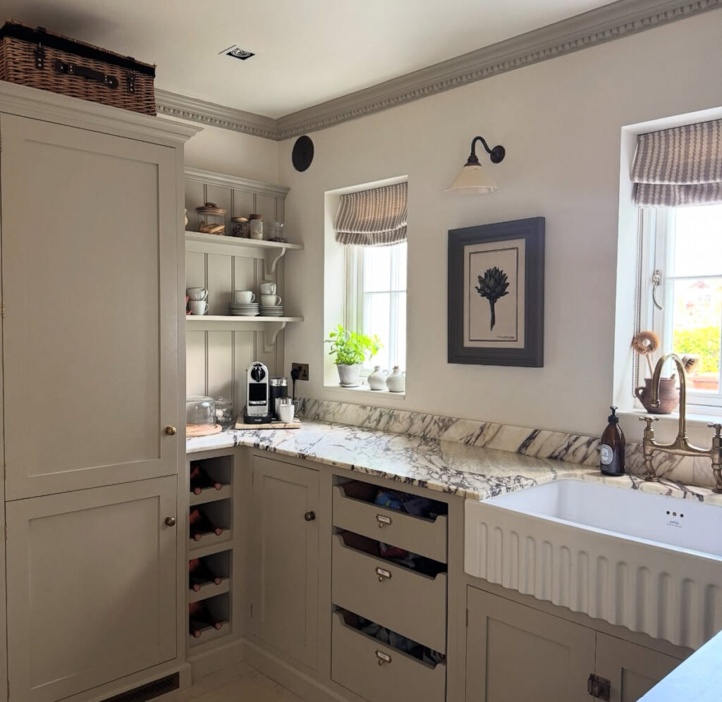 light neutral kitchen corner with marble countertop and farmhouse sink leading into a walk in pantry style storage nook