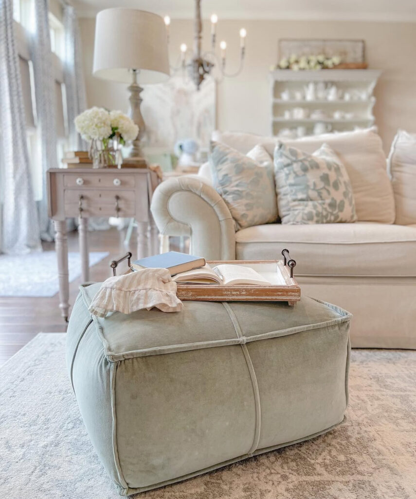 A velvety mint pouf, rolled-arm sofa, and carved side table form a relaxed corner anchored by classic french country chairs.