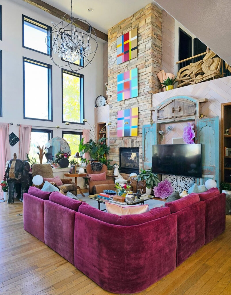 Loft living room with fuchsia velvet sectional and tall stone fireplace, a vibrant showcase of modern eclectic home decor energy.