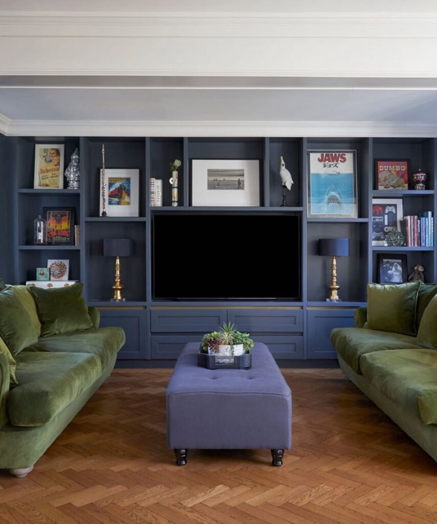 Navy built-in shelves filled with art and books surrounding a central television, rich living room tv wall ideas for homes that love color.
