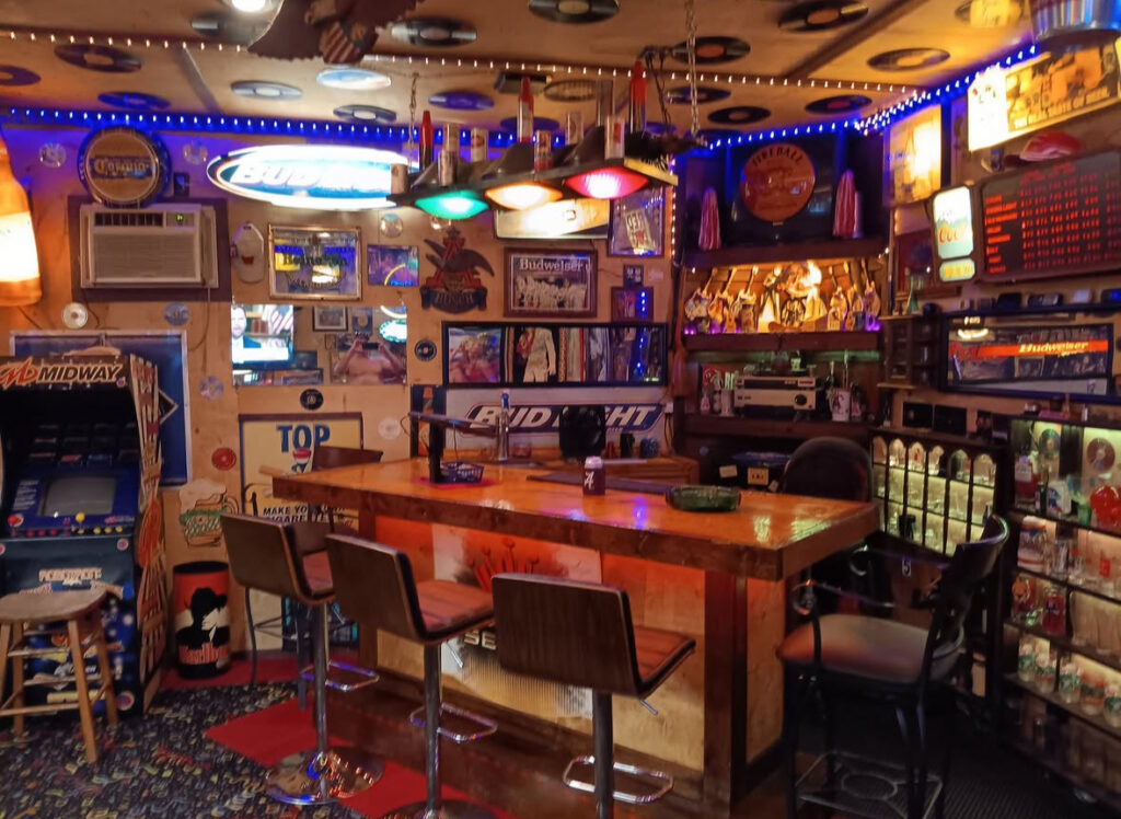 Colorful neon signs, arcade machines, and a wood bar create a lively man cave garage bar packed with memorabilia.