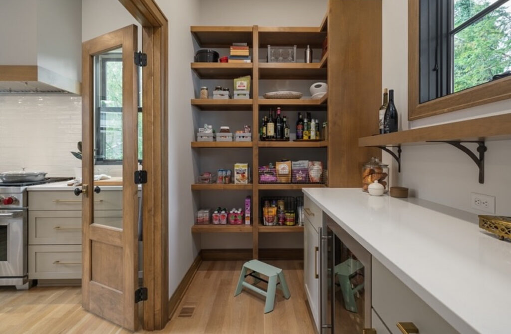 wood framed door leads into an oak shelving lined walk in kitchen pantry with a long white counter and window