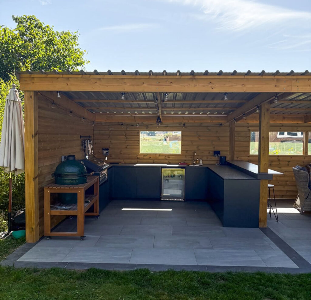 Wood-clad shelter with L-shaped counters, grill, and kamado cooker presenting cozy backyard covered outdoor kitchen ideas