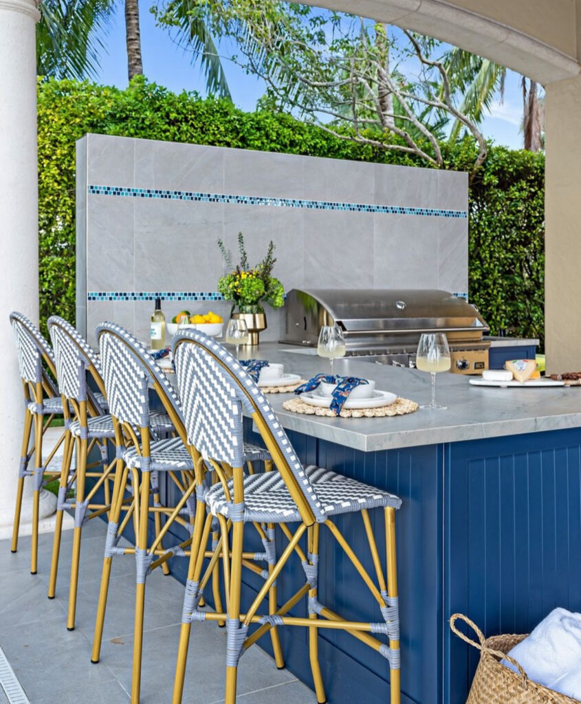 Blue island with bar stools facing the pool and integrated grill wall showing a social outdoor kitchen layout