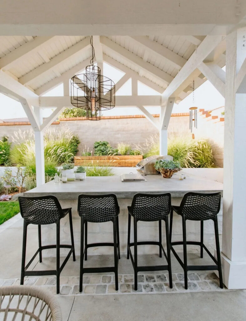 White gabled pavilion with concrete bar and black stools illustrating an efficient outdoor kitchen layout