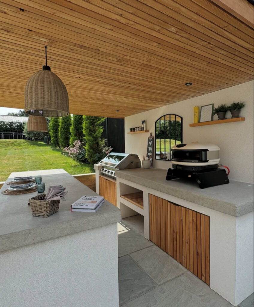 Pavilion with concrete counters, grill, pizza oven, and bar island arranged in a social outdoor kitchen layout