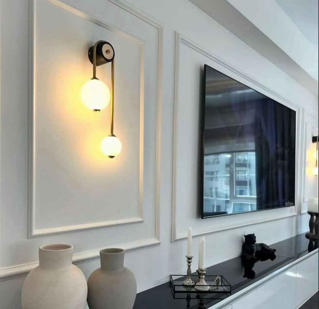 Elegant white paneled wall, glowing sconce, and sleek console create subtle living room accent wall ideas with tv in a modern apartment.