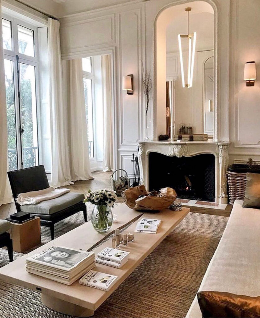 Carved armchairs and a low modern table sit beneath tall paneled walls, highlighting elegant french country chairs in a refined space.