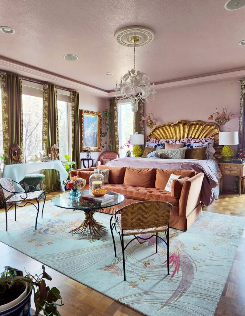 Romantic pink bedroom with gold shell headboard, velvet sofa, and ornate chandelier, celebrating luxurious vintage eclectic home decor.