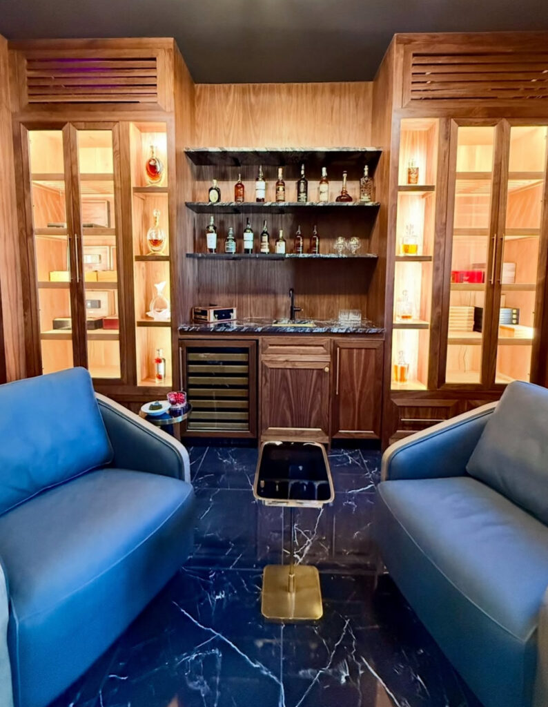 Warm wood cabinetry, lit bottle displays, and marble floors offer elegant man cave wall ideas for showing off a whiskey collection.