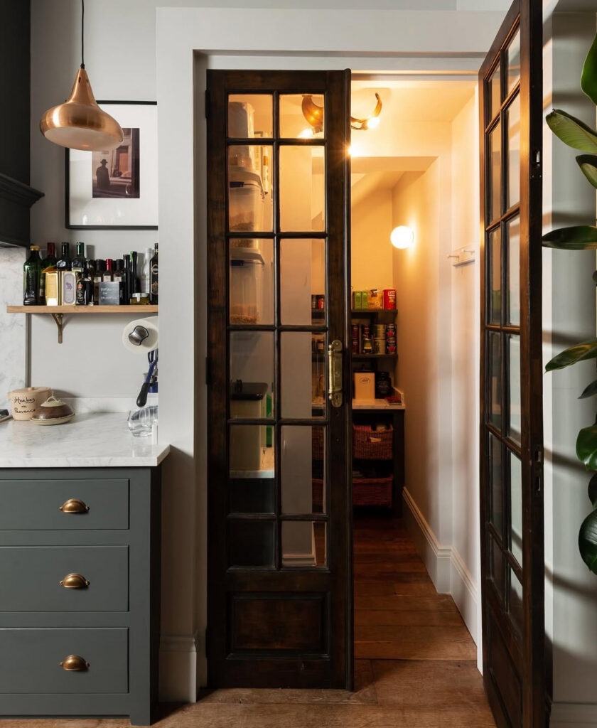 dark wood glass door opens from the kitchen into a hidden small walk in pantry tucked under the stairs