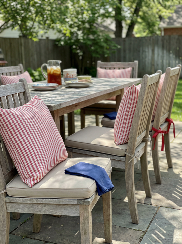 Outdoor decorations with a patio dining table, decorative pillows in red white blue stripes, and simple table decor for a relaxed backyard setup.