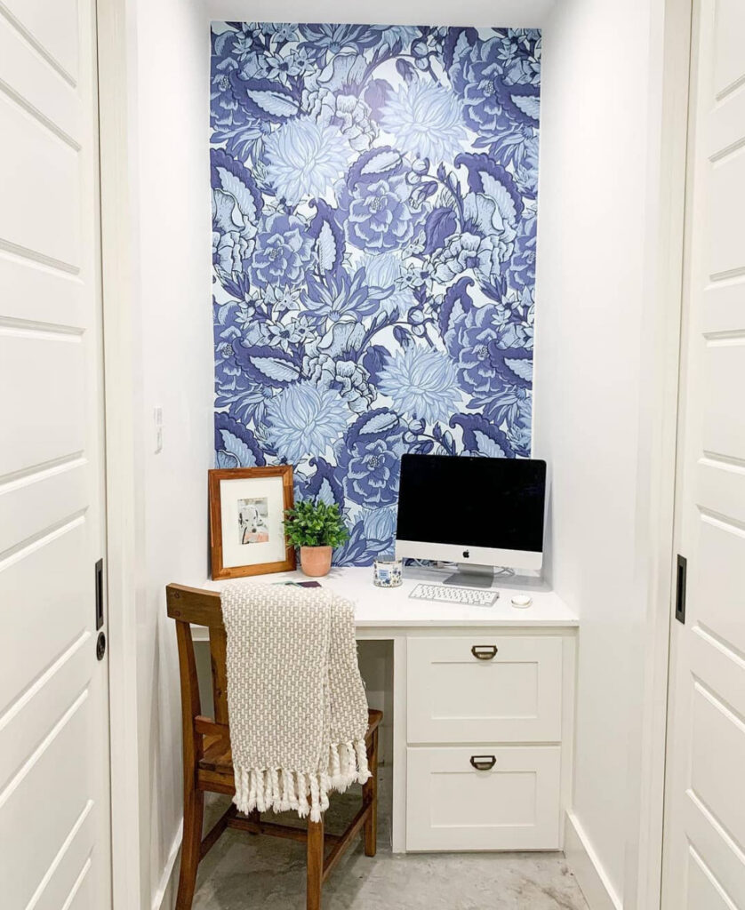 Tiny niche desk framed by bold blue floral wallpaper and clean white cabinetry, home office decor with big personality.