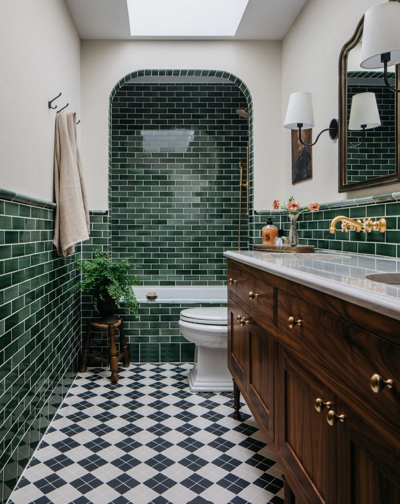 Long room with an arched tub alcove clad in emerald subway tiles, epitomizing a luxurious vintage green tile bathroom.
