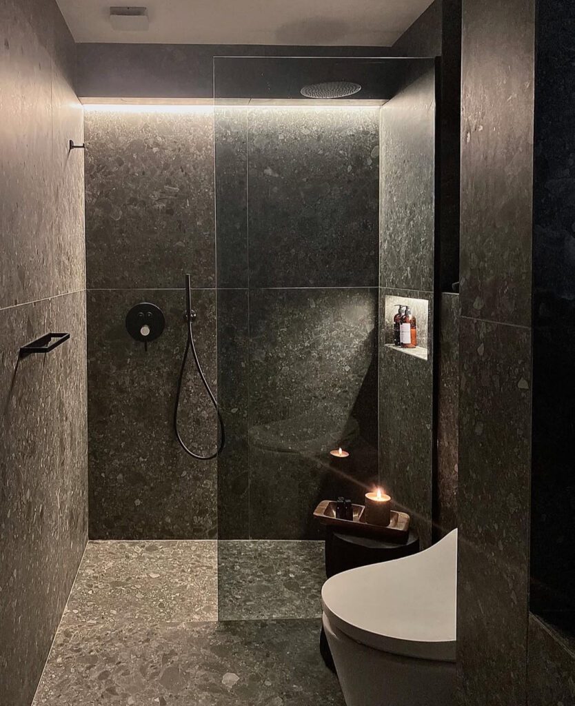 Stone-wrapped bath with candles and minimal fixtures creating a soothing black accent bathroom.