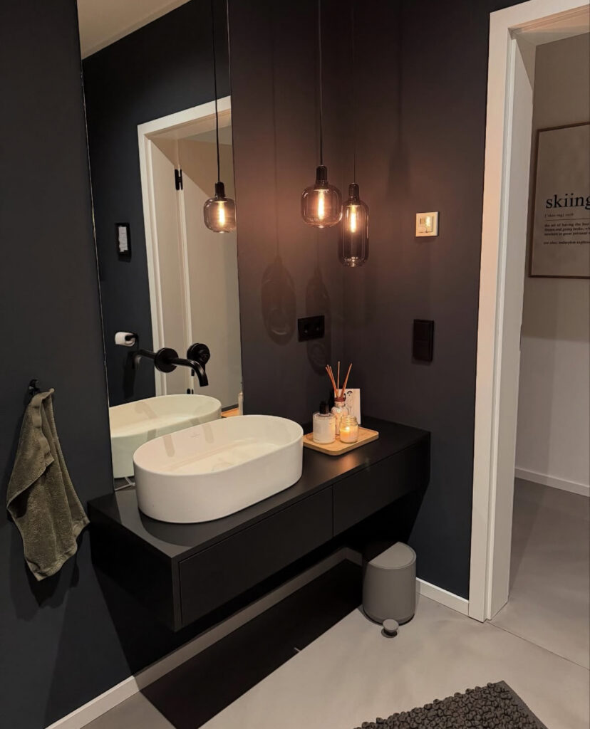 Floating black vanity with gold pendant lights and white basin showing a black bathroom contrast style.