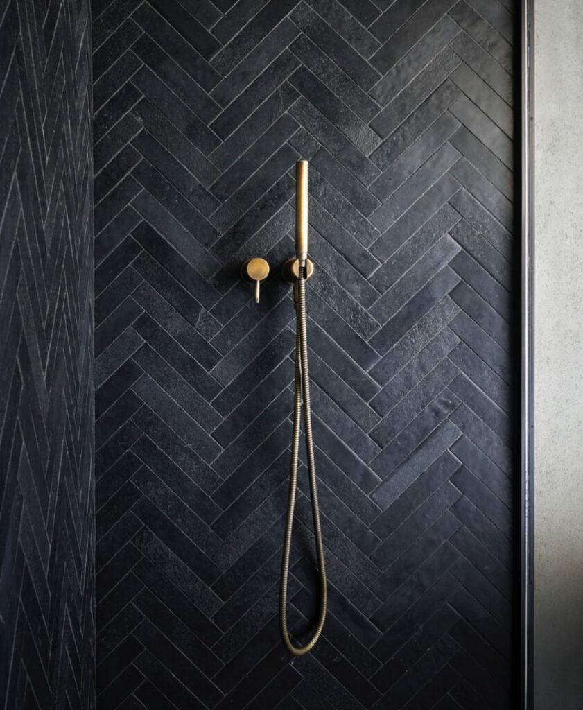 Chevron limestone shower with brass fixture focusing on black bathroom textures.