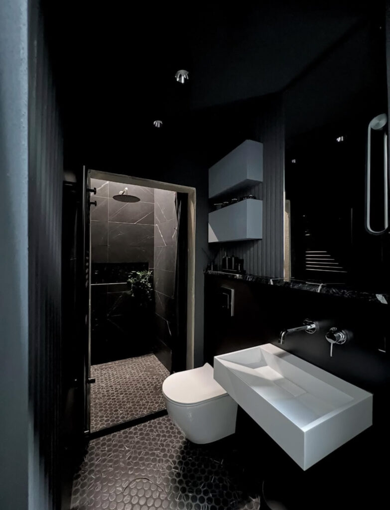 Deep black bathroom with textured stone floor and slatted wood walls emphasizing black bathroom textures.