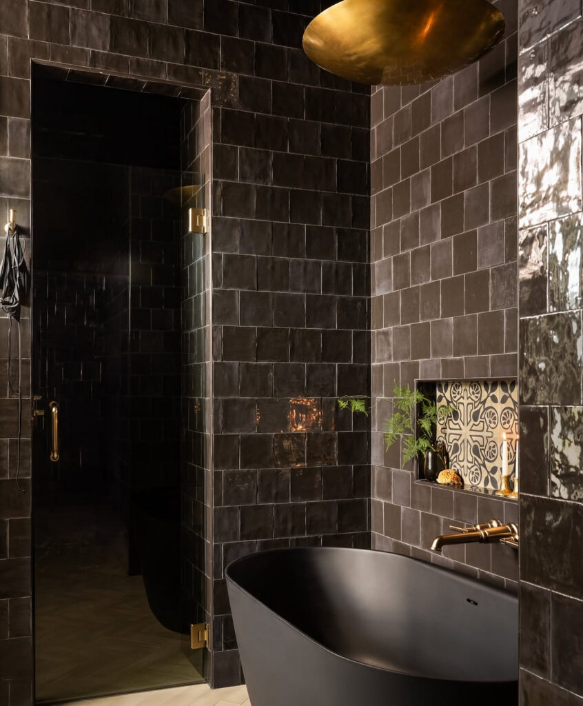 Glossy black tiles and brass ceiling light creating a luxurious black bathroom with gold look.