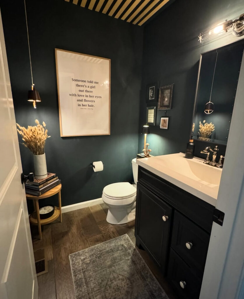 Minimal black painted bathroom with art, dried stems, and a wood floor highlighting a black paint bathroom look.