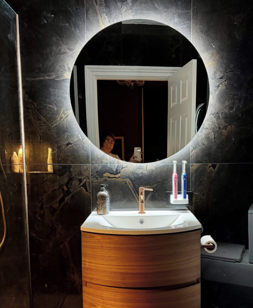 Small ensuite with dark stone wall and glowing mirror featuring black tiles for bathroom inspiration.