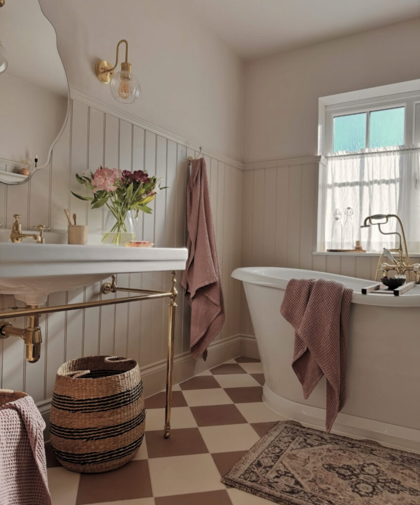 Warm neutral space with pink towels, brass fixtures, and a checkerboard floor showcasing charming vintage bathroom ideas.