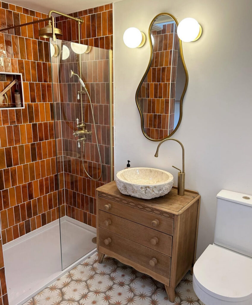 Colorful bathroom ideas with bold terracotta shower tile, a vintage-style wood vanity, and warm brass bathroom fixtures.