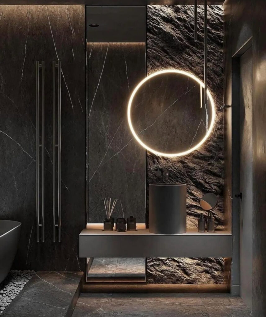 Dark stone bathroom with glowing ring mirror and sleek sink representing a bold black bathroom design.
