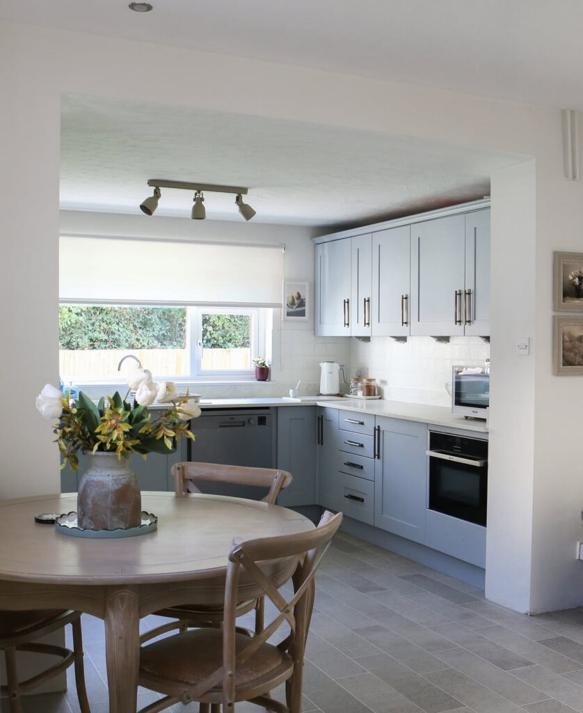 Bright kitchen with soft blue cabinets, black hardware and pale floors, plus a cosy round dining table, updated by @lizaprideaux.