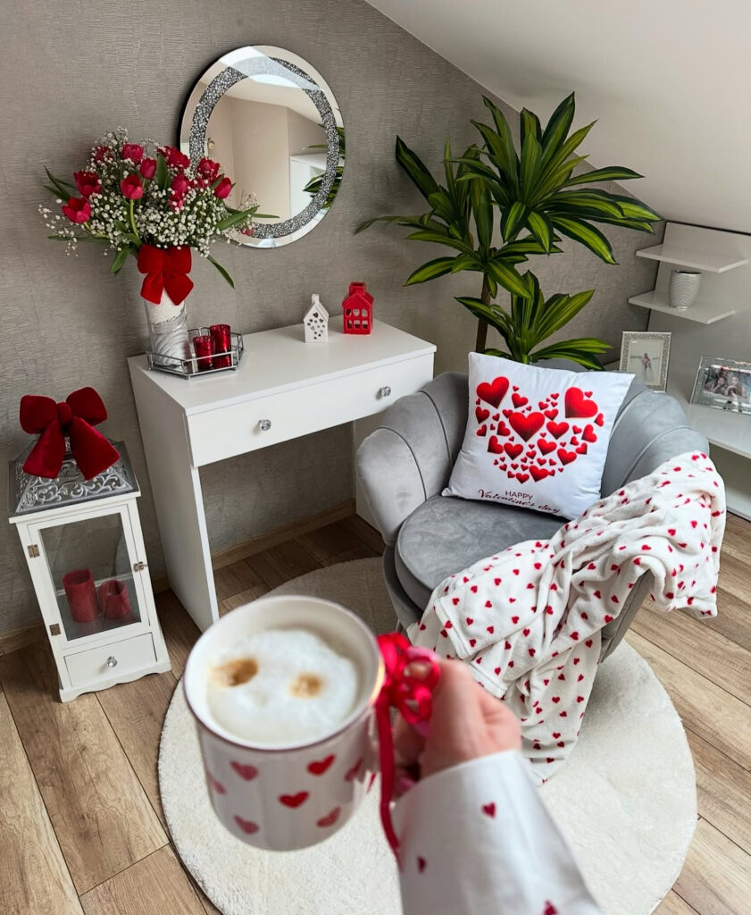 Small cozy corner with a heart pillow, coffee mug, and red flowers highlighting valentines room decor simplicity.