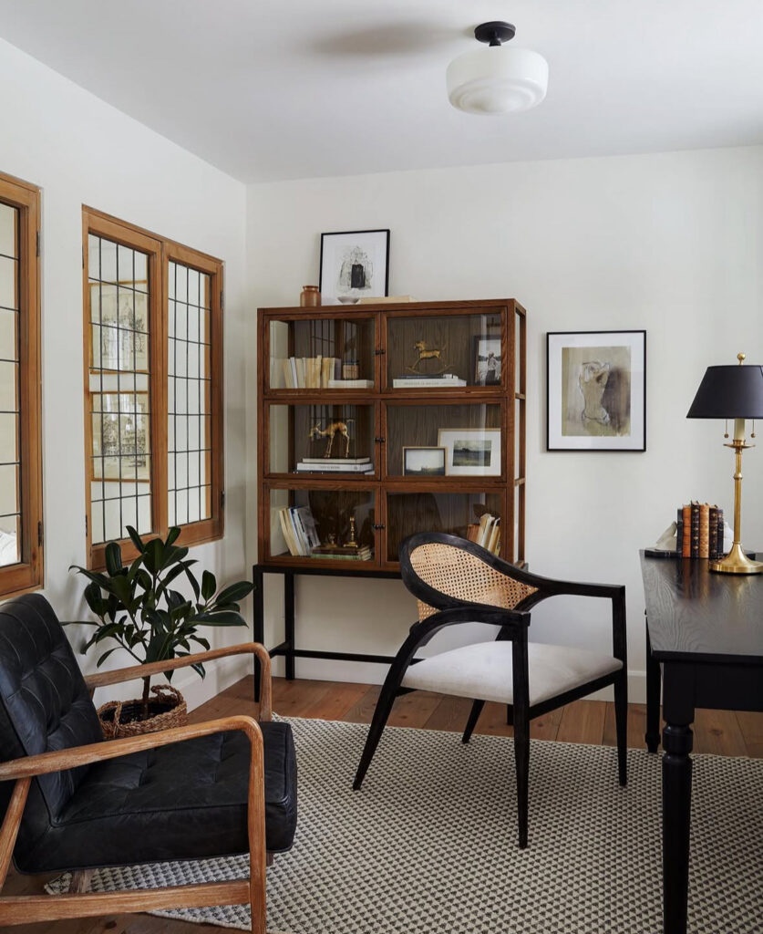 Living room office corner styled with a glass-front cabinet, layered art, and warm wood tones, cozy home office energy.