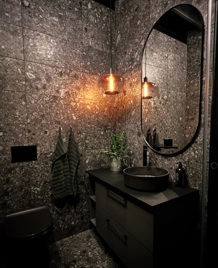 A dark, stone-wrapped bathroom with warm amber pendant lights capturing a dark bathroom design.