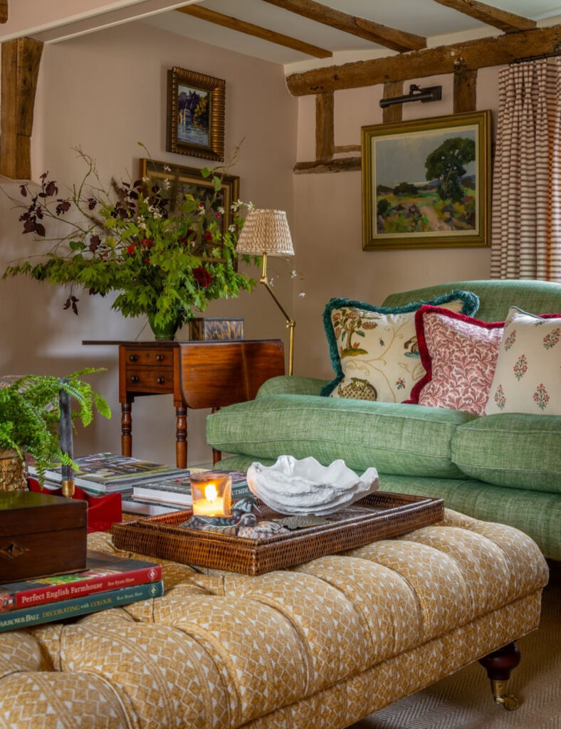Eclectic retro 70s living room with green roll arm sofa, tufted ottoman, floral cushions and rustic beams.