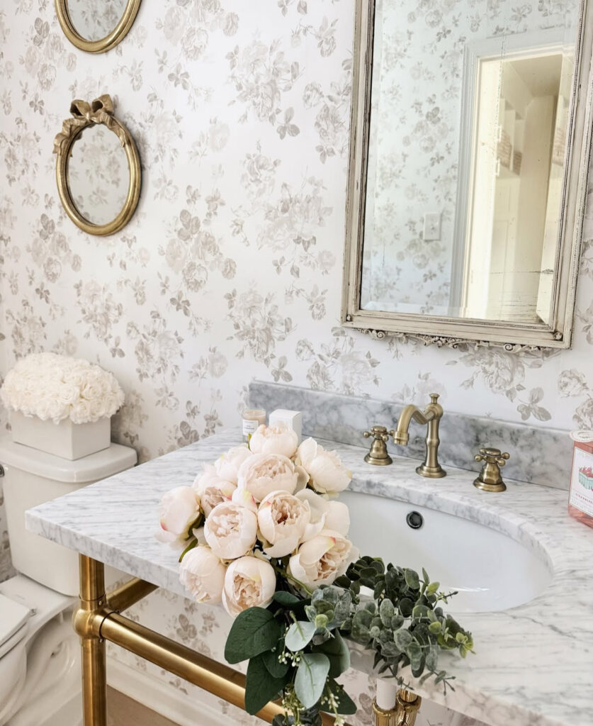 Romantic floral powder room with marble console sink and ornate gold vintage bathroom mirror.