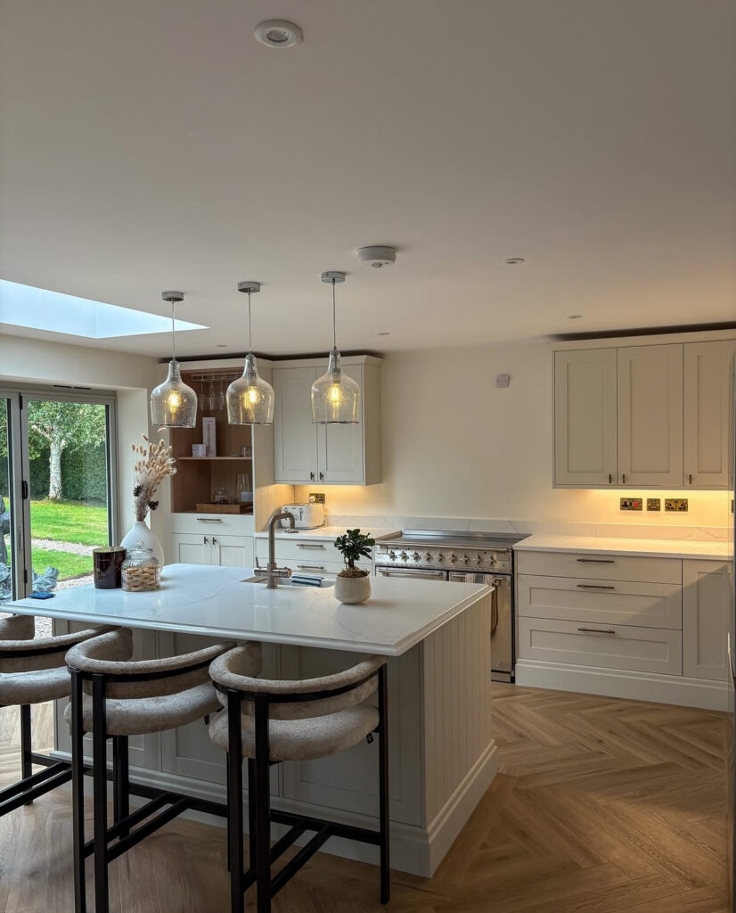 Bright open-plan kitchen with a large white kitchen island, herringbone wood floors and a defined dining area creating better kitchen flow, designed by @ourluxehome_.
