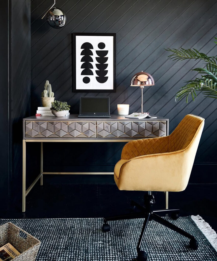 Moody black paneled wall with geometric-front desk, warm lamp glow, and mustard chair, functional workspace with drama.