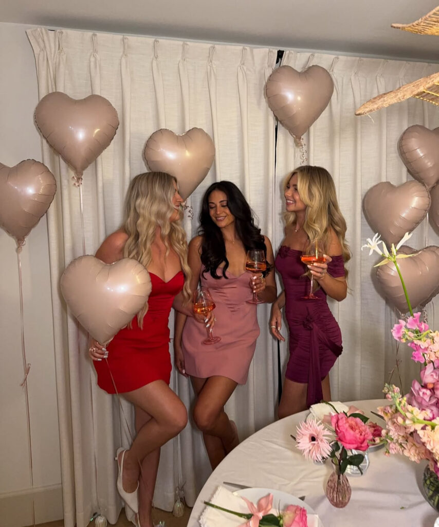 Group of women in pink and red Galentine’s outfits posing with heart balloons at a Galentine’s Day party